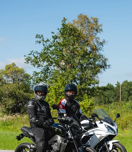 Två motorcyklister på en landsväg omgiven av grönt landskap