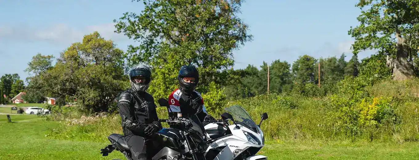 Två motorcyklister på en landsväg omgiven av grönt landskap